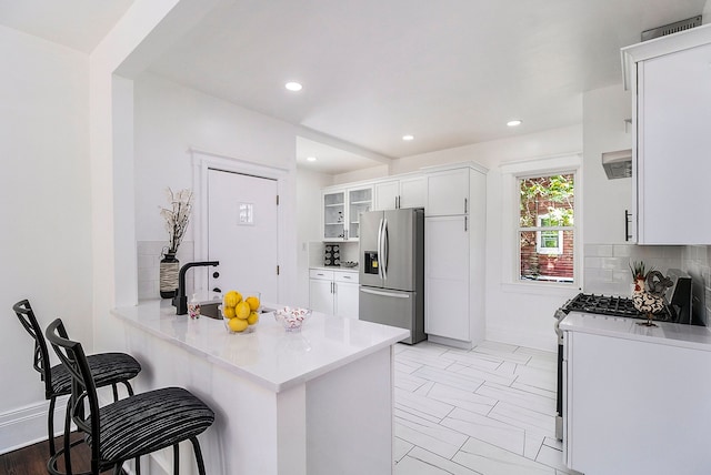 kitchen with stainless steel fridge with ice dispenser, kitchen peninsula, a breakfast bar area, decorative backsplash, and white cabinets