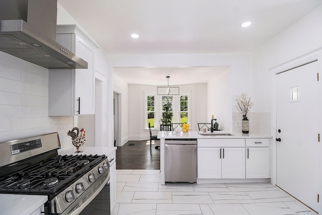 kitchen with wall chimney exhaust hood, stainless steel appliances, sink, decorative light fixtures, and white cabinets