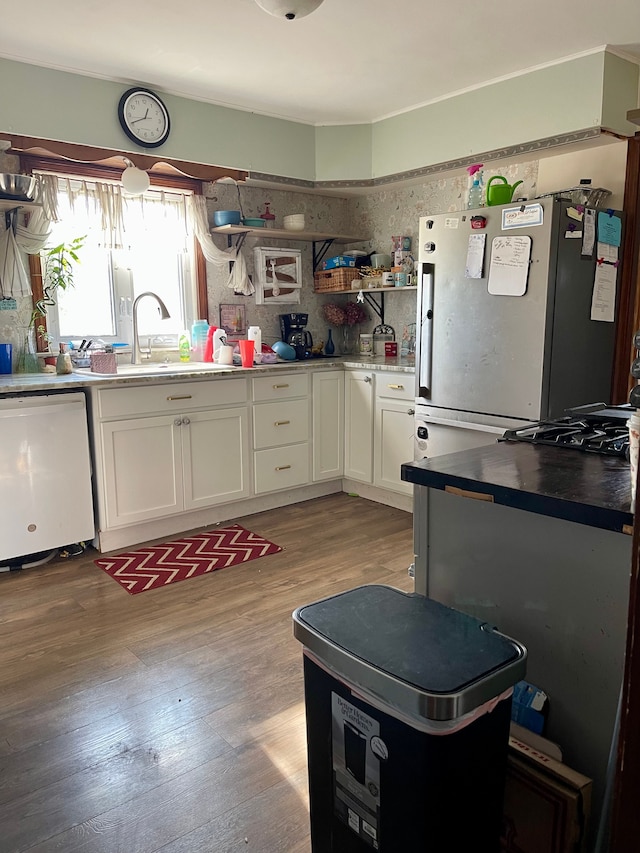 kitchen featuring sink, dishwasher, white cabinets, light hardwood / wood-style floors, and stainless steel refrigerator