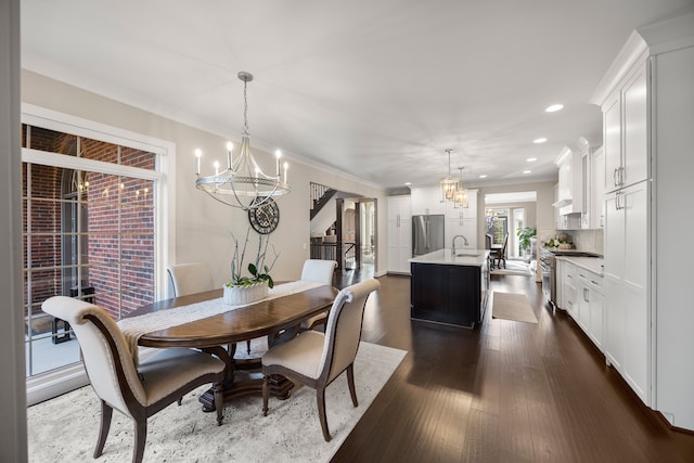 dining space with dark hardwood / wood-style flooring, ornamental molding, sink, and an inviting chandelier