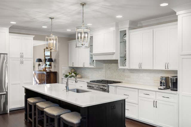 kitchen with sink, an island with sink, decorative light fixtures, white cabinets, and appliances with stainless steel finishes