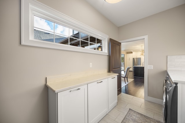 kitchen featuring light hardwood / wood-style floors, washer / dryer, white cabinetry, and light stone counters