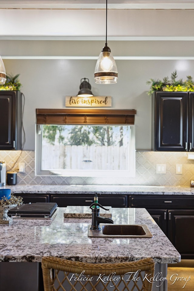 kitchen with decorative backsplash, sink, light stone countertops, and decorative light fixtures