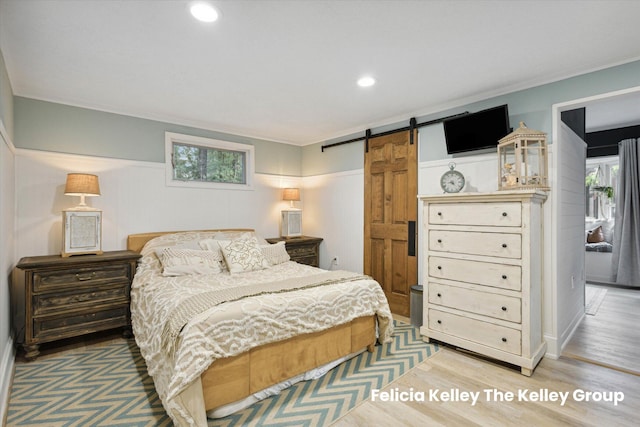 bedroom featuring a barn door, wood-type flooring, and crown molding