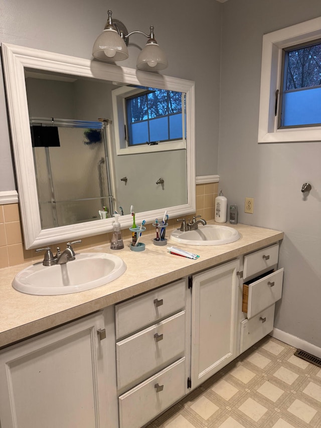 bathroom featuring vanity, a shower with shower door, and decorative backsplash