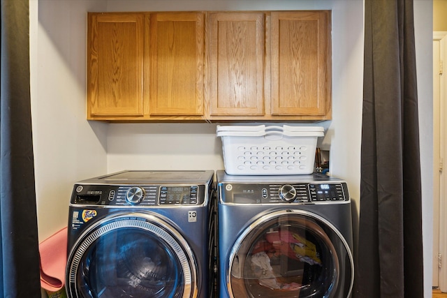 clothes washing area with washing machine and clothes dryer and cabinets