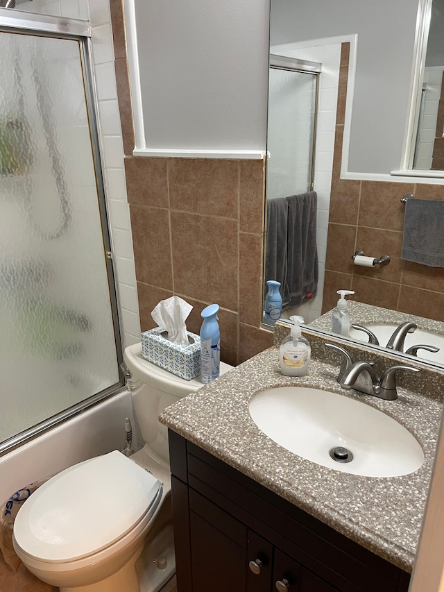 full bathroom featuring vanity, toilet, tile walls, and combined bath / shower with glass door