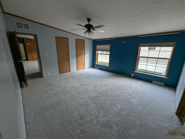 carpeted spare room featuring a textured ceiling, vaulted ceiling, ceiling fan, and a healthy amount of sunlight