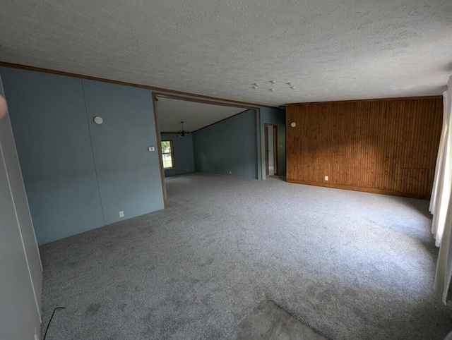 carpeted spare room featuring a textured ceiling and wood walls