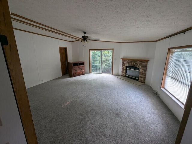 unfurnished living room with carpet, crown molding, ceiling fan, a fireplace, and a textured ceiling