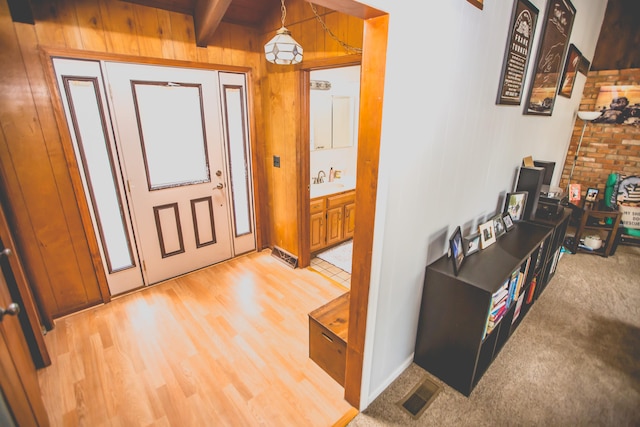 entrance foyer with beam ceiling, wood walls, and sink