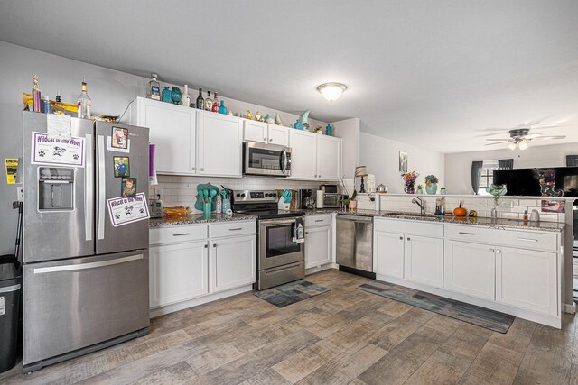 kitchen featuring sink, stainless steel appliances, dark stone countertops, hardwood / wood-style floors, and white cabinets