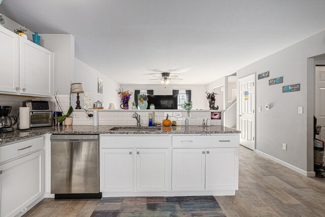 kitchen with stainless steel dishwasher, white cabinets, sink, and dark stone counters