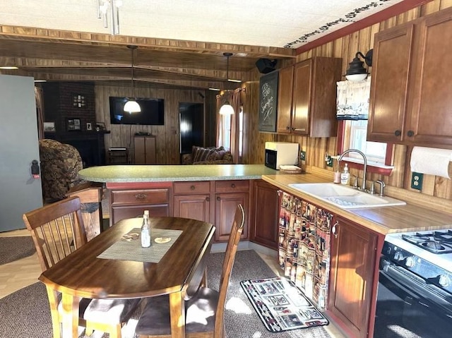 kitchen featuring kitchen peninsula, black range with gas stovetop, wood walls, and sink