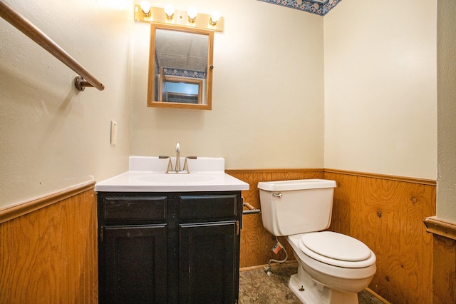 bathroom with vanity, toilet, and wood walls