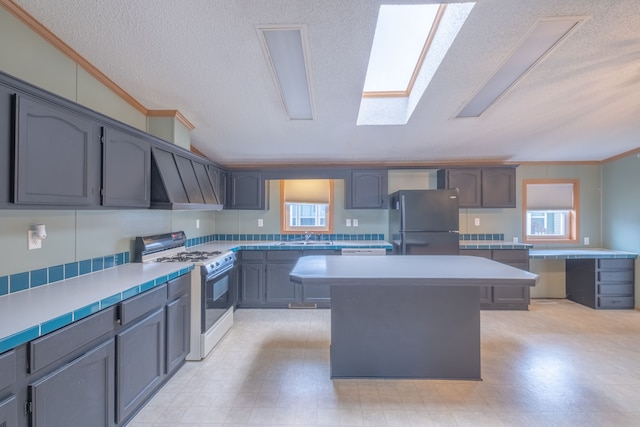 kitchen with black refrigerator, wall chimney exhaust hood, a textured ceiling, a kitchen island, and white range with gas cooktop