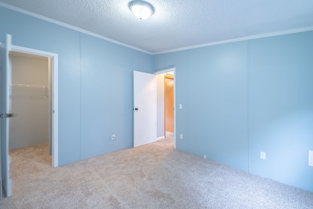 unfurnished bedroom featuring a spacious closet, carpet floors, a textured ceiling, and ornamental molding