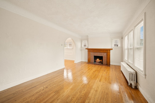 unfurnished living room featuring radiator heating unit, a brick fireplace, crown molding, a textured ceiling, and light wood-type flooring