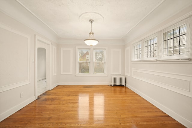 unfurnished dining area featuring hardwood / wood-style floors, crown molding, radiator, and a textured ceiling