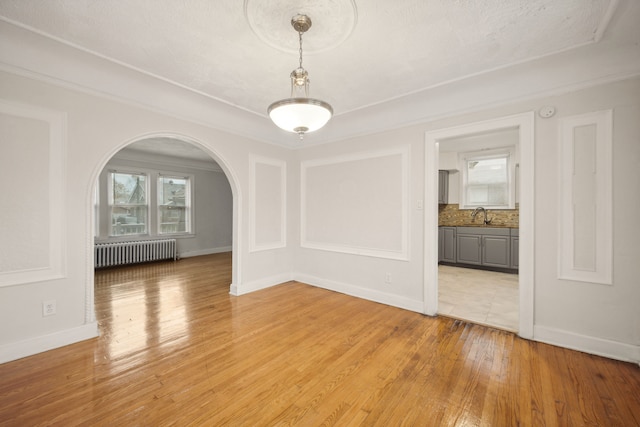 unfurnished dining area with a textured ceiling, light hardwood / wood-style floors, sink, and radiator