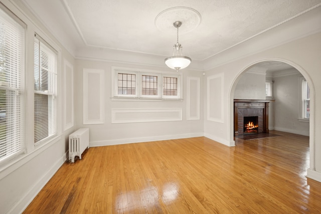 unfurnished living room featuring radiator heating unit, a brick fireplace, ornamental molding, and wood-type flooring