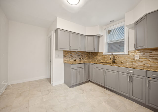 kitchen with gray cabinetry, decorative backsplash, stone countertops, and sink