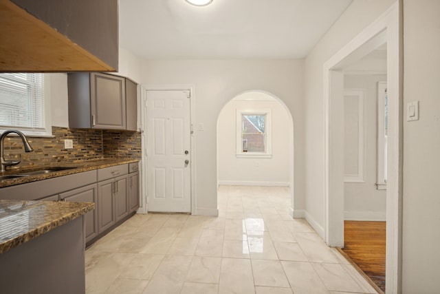 kitchen featuring sink, backsplash, gray cabinetry, and dark stone countertops