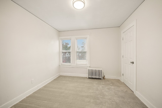 spare room featuring light carpet and radiator heating unit