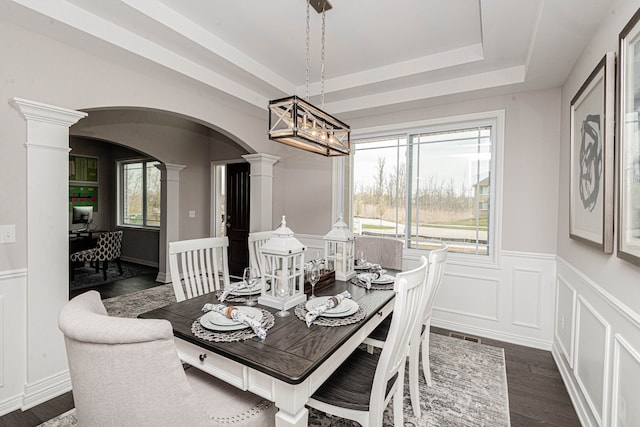 dining space with dark wood-type flooring, a tray ceiling, and decorative columns