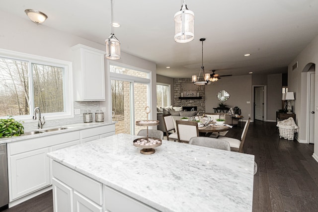 kitchen featuring sink, hanging light fixtures, white cabinets, a kitchen island, and a stone fireplace