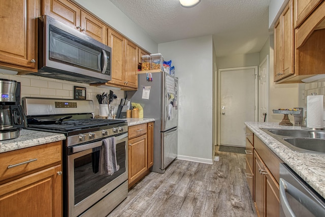 kitchen with light stone countertops, light hardwood / wood-style flooring, a textured ceiling, and appliances with stainless steel finishes