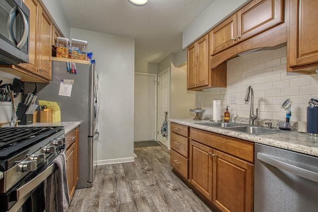 kitchen featuring sink, wood-type flooring, a textured ceiling, decorative backsplash, and appliances with stainless steel finishes