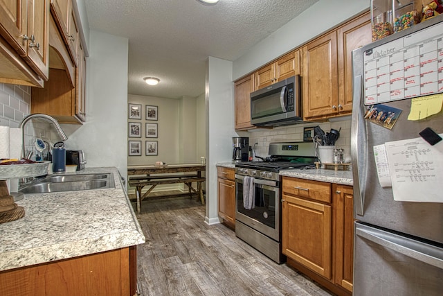 kitchen featuring sink, stainless steel appliances, tasteful backsplash, a textured ceiling, and hardwood / wood-style flooring