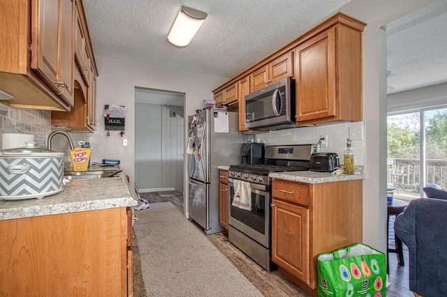 kitchen featuring tasteful backsplash, light hardwood / wood-style floors, a textured ceiling, and appliances with stainless steel finishes