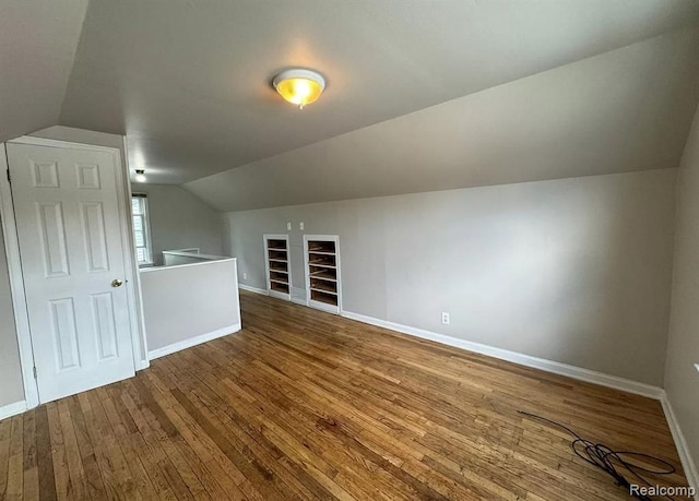 additional living space featuring built in shelves, lofted ceiling, and hardwood / wood-style flooring