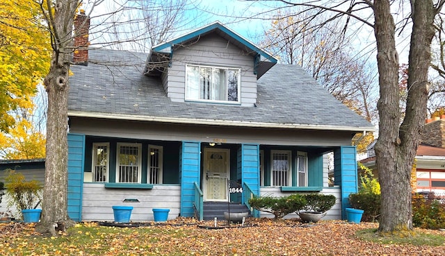 bungalow-style home with covered porch, a chimney, and roof with shingles