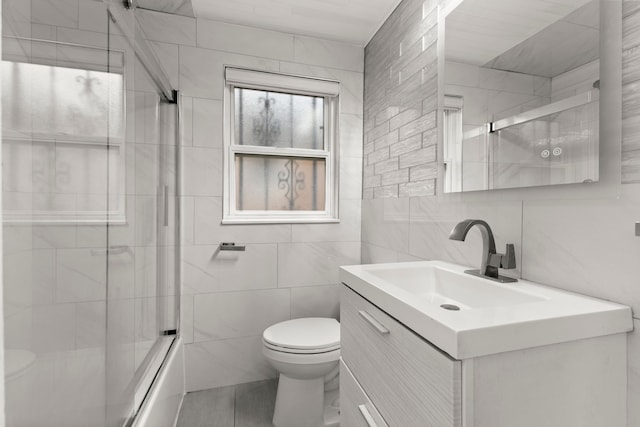 full bathroom with shower / bath combination with glass door, vanity, toilet, and tile walls