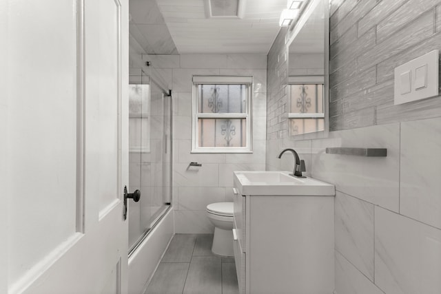 full bathroom with vanity, tile patterned floors, bath / shower combo with glass door, toilet, and tile walls