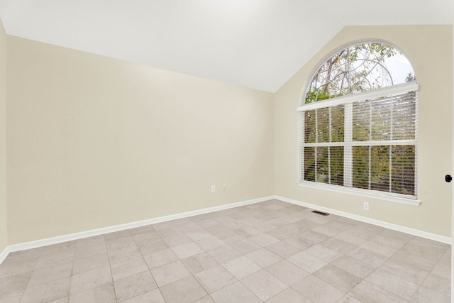 spare room featuring vaulted ceiling and light tile patterned flooring