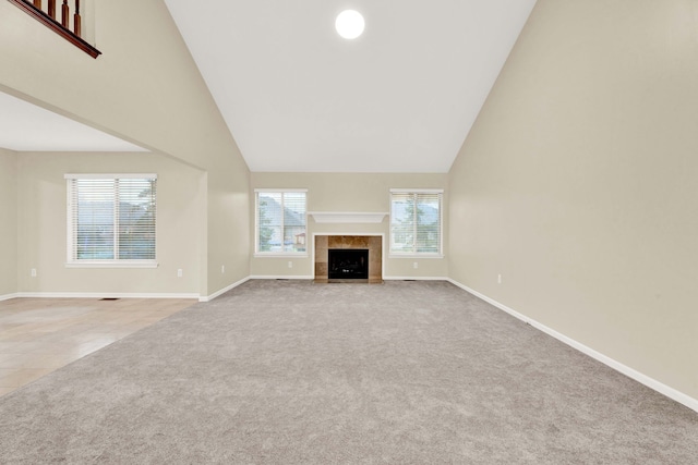 unfurnished living room featuring a tile fireplace, high vaulted ceiling, and light colored carpet