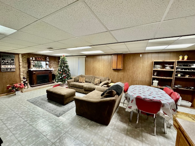 living room with a paneled ceiling, wood walls, and a brick fireplace