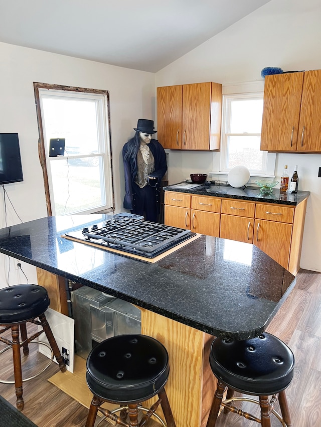 kitchen featuring a kitchen bar, wood-type flooring, gas stovetop, and lofted ceiling