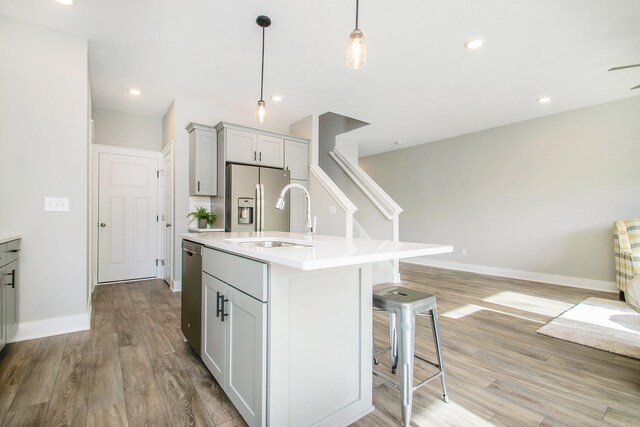 kitchen with pendant lighting, a kitchen island with sink, sink, light wood-type flooring, and appliances with stainless steel finishes