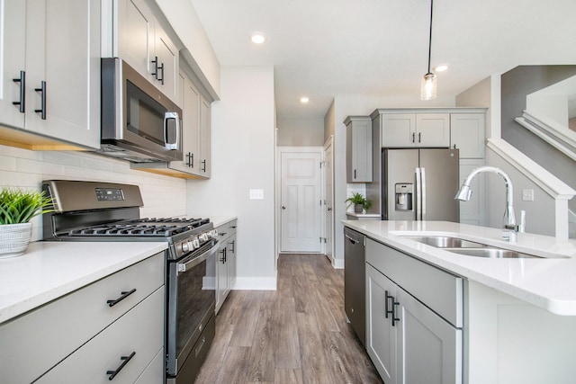 kitchen with gray cabinetry, sink, hardwood / wood-style flooring, decorative light fixtures, and stainless steel appliances