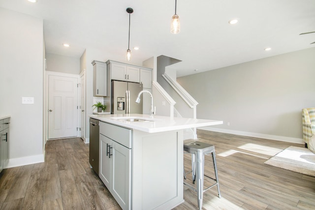 kitchen with appliances with stainless steel finishes, sink, hanging light fixtures, a center island with sink, and light wood-type flooring