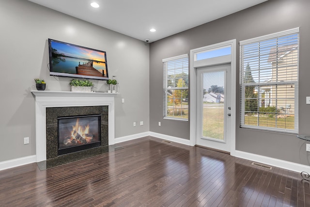 unfurnished living room featuring a premium fireplace, dark wood-type flooring, and a wealth of natural light