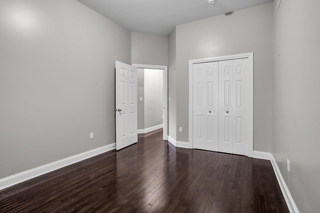 unfurnished bedroom featuring dark hardwood / wood-style flooring, a towering ceiling, and a closet