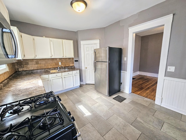 kitchen featuring gas stove, tasteful backsplash, stainless steel fridge, white cabinets, and light wood-type flooring