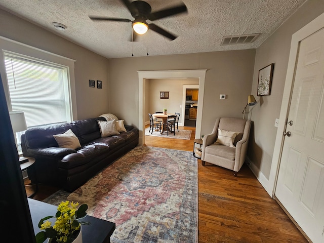 living room with a textured ceiling, dark hardwood / wood-style flooring, and ceiling fan