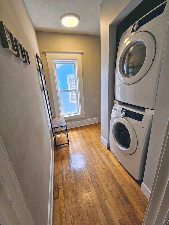 washroom with a textured ceiling, light hardwood / wood-style flooring, and stacked washer and clothes dryer